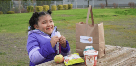 small girl eating lunch on a wooden table outside