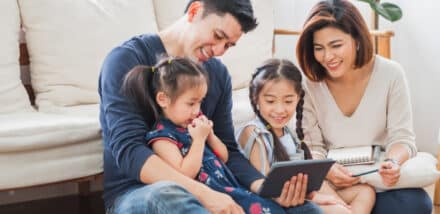 smiling family looking at screen while sitting on the living room floor